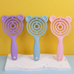 Three bear-ear shaped hair brushes in purple, blue, and pink on a textured white base