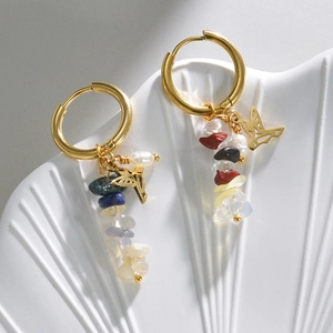 Detail of 14k gold hoops with bird charms and multi-color natural stones on ceramic