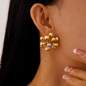Détail de la boucle d'oreille fleur dorée avec perle violette sur l'oreille d'un modèle