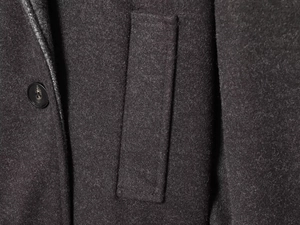 Detailed macro view of dark grey wool coat featuring pocket flap and single-breasted button