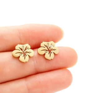 Gold stainless steel hibiscus flower earrings shown on fingertip for size reference