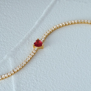 Détail du bracelet en chaîne dorée avec zircons pavés et une pierre centrale en cœur rouge
