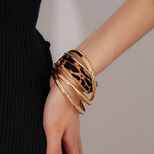 Gros plan de bracelets dorés superposés avec cuir imprimé léopard au poignet femme