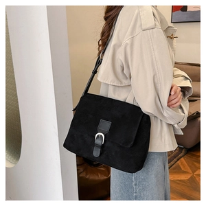 Close-up of black faux suede crossbody bag with flap and metal buckle on beige trench coat