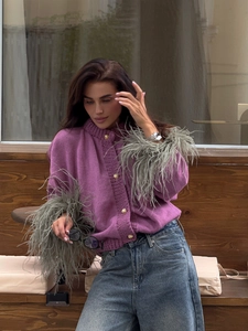 Close-up of purple knit cardigan featuring faux feather cuffs and gold embossed buttons