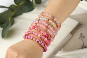 Nahaufnahme der mehrlagigen Perlenarmband-Sets mit roségoldenem Kronenanhänger in Rosa