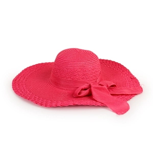 Close-up of rose red straw sun hat with ribbon bow detail and woven texture on white background
