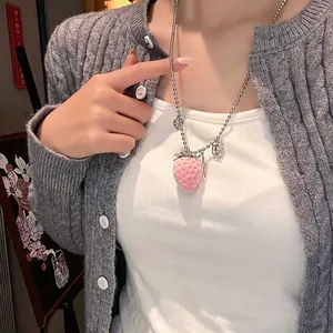 Close-up of pink flocked strawberry pendant on a silver beaded chain worn by a model