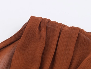 Detail der rotbraunen Faltenstoff-Textur auf dem V-Ausschnitt Kleid für weiche Haptik