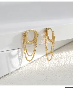 Macro shot of gold hoop earrings with zircon stones and flowing tassel chains on white decor