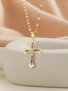 Detailed shot of golden cross pendant with colorful zircon stones on white ceramic