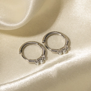 Orecchini a cerchio in argento lucido con tre piccole perle su elegante tessuto beige