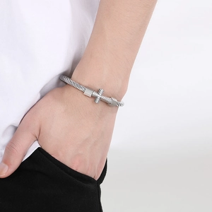 Detail of silver twisted cable cuff bracelet with cross charm on a woman's wrist