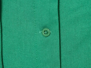 Macro detail of natural linen blend fabric with button on a green sleeveless maxi dress