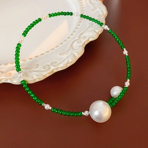 Detail of beaded necklace with green gemstone beads and large white pearls on a ceramic plate