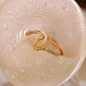 Close-up of 18K gold wave ring with a white pearl on a wet textured surface
