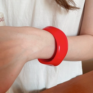 Close-up of wide red acrylic resin bangle with a pleated geometric design on a wrist