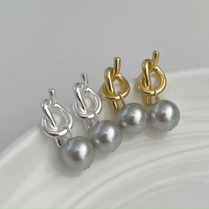 Detail of silver and gold knotted earrings with grey pearls on white ceramic