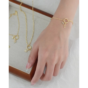 Detail of gold evil eye and cross pendants on link bracelet with T-bar clasp