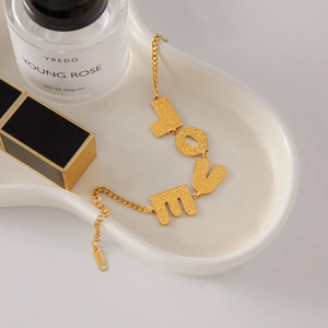 Close-up of golden LOVE letter bracelet on porcelain tray with textured metal details