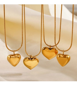 Detail of four gold heart pendants on snake chains over elegant folded fabric