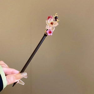 Detailed view of pink flower hair pin with dark wood stick and golden leaf tassels