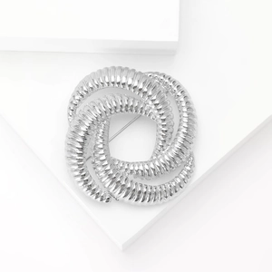Close-up of a silver geometric knot brooch featuring a sophisticated twisted metal texture