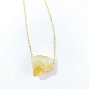 Detailed macro view of an irregular yellow raw crystal stone pendant on a gold thin chain