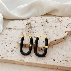 Detail of gold U-shaped earrings with black enamel on beige travertine and white silk