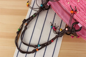 Détail d'un sac à bandoulière en paille rose avec perles colorées sur une sangle