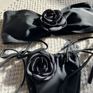 Detail of black bandeau bikini featuring large 3D fabric rose and side-tie bottoms