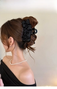Détail d'une pince à cheveux élégante en satin noir plissé portée sur un chignon chic
