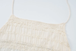 Détail du tissu à volants blanc crème et bretelles spaghetti sur un haut dos nu cintré