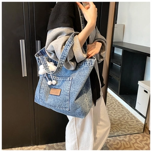 Detail of light blue denim tote bag with brown leather tag and plush white charm
