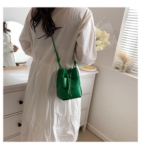 Lifestyle view of a green hand-woven bucket bag worn with a white dress in a bright room