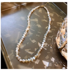 Detail of baroque freshwater pearl necklace with gold clasp on reflective tray