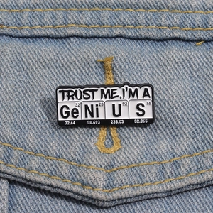 Detail of periodic table enamel pin saying Genius pinned on a blue denim jacket