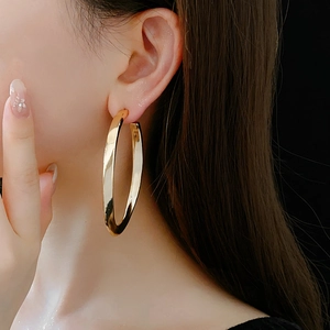 Close-up of model wearing large oval golden hoop earrings with high-gloss metallic finish