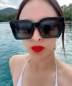 Close-up of stylish black square sunglasses worn by a model in a coastal setting