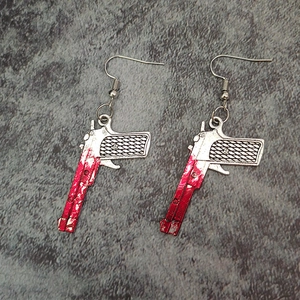 Detailed view of silver pistol earrings with realistic red blood splatters and ear hooks