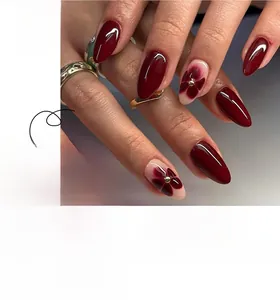 Détail d'ongles en amande bordeaux avec motifs floraux délicats et petites perles dorées