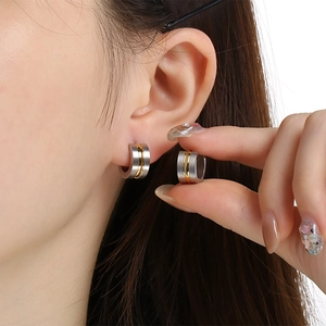 Close-up of minimalist C-shaped brushed steel earring with gold stripe on human ear