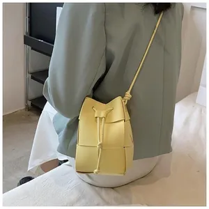 Detail of a mini yellow woven bucket bag with drawstring and shoulder strap on a model