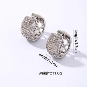 Close-up of wide silver huggie earrings with pave-set zircons and hollow patterns