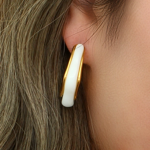 Detail of white enamel U-shaped earrings with gold trim worn by a female model