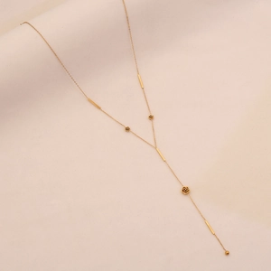 Dettaglio della collana a Y dorata con ciondoli a rosa ed elementi geometrici su fondo crema