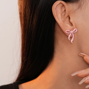 Close-up of pink bow stud earring with a glossy finish on woman's earlobe