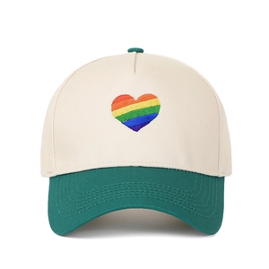 Dettaglio del ricamo a cuore arcobaleno su un cappellino bicolore beige e verde scuro