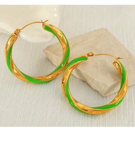 Detailed close-up of gold-plated twisted hoop earrings with green enamel on a stone base