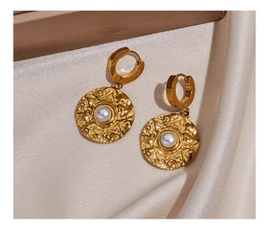 Detail of gold hammer-textured pearl drop earrings resting on champagne silk fabric
